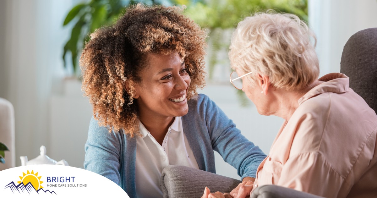 A caregiver smiles at an older client in a chair, representing the joy that can come from a healthy work-life balance.