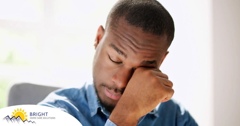 A man tiredly rubs his eyes, representing the exhaustion that can come with family caregiving.