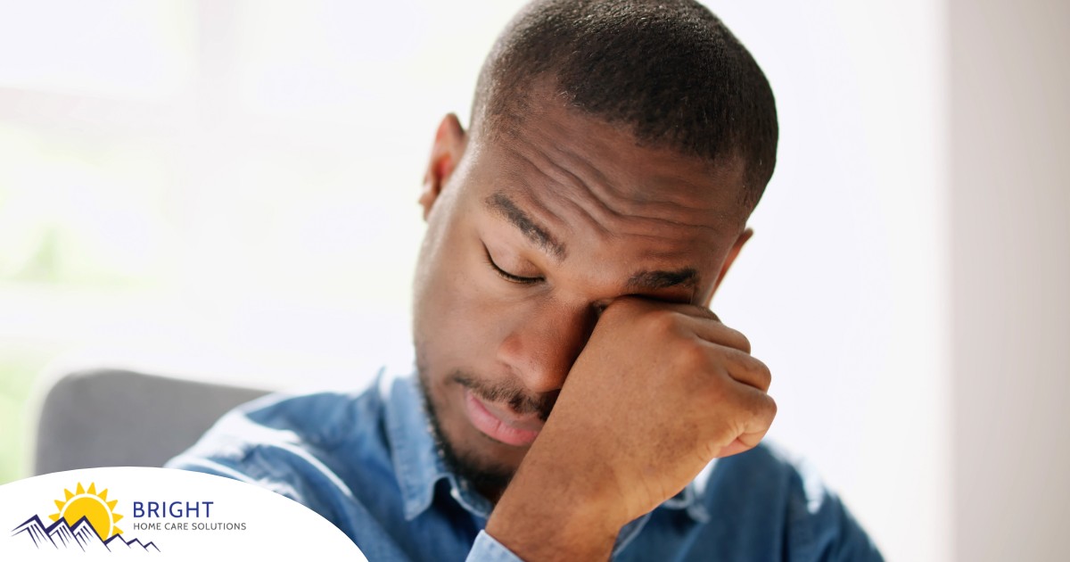 A man tiredly rubs his eyes, representing the exhaustion that can come with family caregiving.